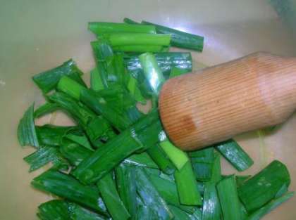 Нарежьте зеленый лук крупными кусками, сложите в миску и подавите толкушкой.