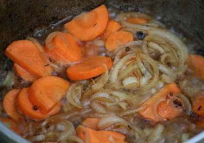 Нарезаем полукольцами лук, а морковь – кружками. Вынимаем из чугунка мясо, на его место для обжарки кидаем лук и морковь, готовим на сильном огне 15 минут.
