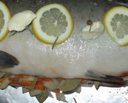 Застелите противень фольгой. На нее следует уложить рыбу. Намажьте рыбу внутри и снаружи заправкой. Затем во внутрь положите нарезанный лук и морковь, добавьте туда же и нашинкованные травы. Воткните в каждый надрез, который вы сделали заранее, кусочки лимона.