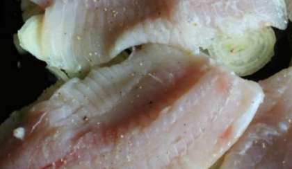 Филе тилапии хорошо промойте. Выложите кусочки филе поверх слоя лука. Рыбу посолите, добавьте специй для рыбы.