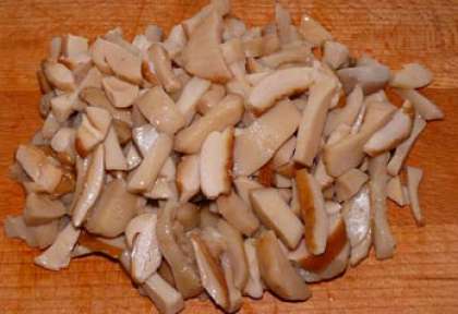 Возьмите баночку с грибами, можно любыми, однако с белыми салат будет вкуснее.  Выложите их в сито. Дайте стечь жидкости, можете промыть (по желанию). Затем нарежьте грибы средними полосками.
