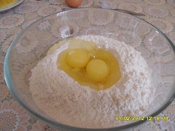 В миске с мукой в середине сделайте отверстие и засыпьте дрожжи,залив их теплой водой. Перемешайте, чтобы дрожжи растворились. Добавьте масло, 2 яйца, половину цедры, и полстакана сахара.