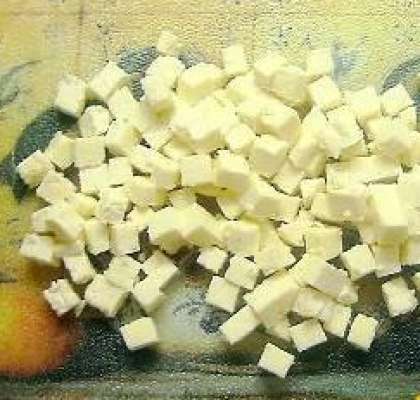 Потом сыр достаньте из упаковки. Слейте воду. Порежьте сыр сначала на ломтики, а  затем каждый из них на средние кубики.