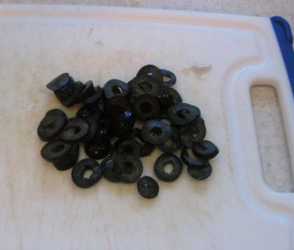 Откройте банку черных маслин. Смотрите, чтобы маслины были без косточек. Нарежьте их небольшими кружечками.