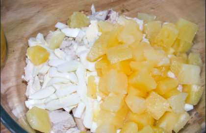 Откройте банку с ананасами. Возьмите глубокую салатницу и соедините нарезанную кубиками курицу, яйцо и ананасы.