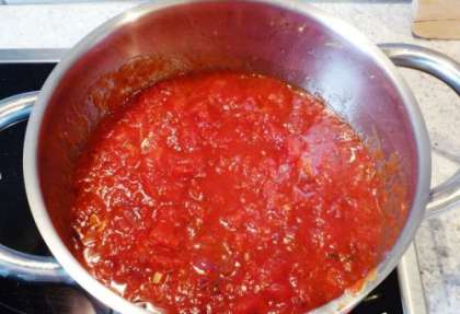 Готовим томатный соус. Для этого нужно мелко нарезать лук и чеснок. Обжариваем в течение минуты сначала лук, а затем чеснок. Жарить нужно в сотейнике или кастрюле с учетом большого объема. Обжаривать лучше до золотистого цвета и появления аромата. Затем выкладываем в кастрюлю томаты в собственном соку, мелко рубленый базилик, соль и перец. Довести соус до кипения, чтобы он немного загустел.