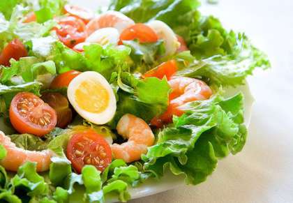 2. Выкладываем листья салата, вареные креветки, помидоры черри и яйца на тарелку, солим и добавляем лимонный сок, согласно рецепту.