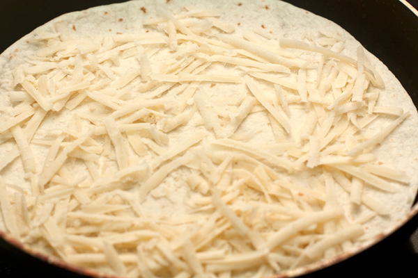 Сыр натрите на крупной терке. Это может быть чеддер, пармезан, гауда или другой твердый или полутвердый сыр. Одну тортилью положите на горячую сухую сковороду, посыпьте ее слоем сыра.