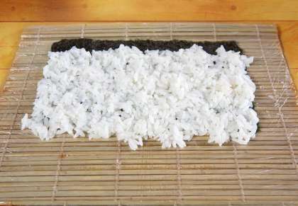 формируя ровный слой риса на листе нори