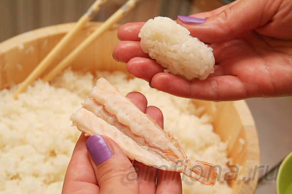 Смочите водой правую ладонь, возьмите небольшое количество риса, прижмите его пальцами, формируя продолговатый комочек. Старайтесь склеить рисинки, не помяв их. На пальцы левой руки положите креветку.