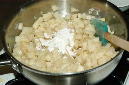 Добавьте нарезанный кубиками картофель и помешайте, чтобы весь картофель был покрыт жиром. Добавьте муку. Перемешайте.
