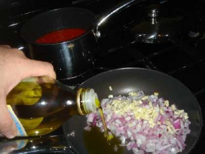 Нарезаем 1/2 красного лука и три зубчика чеснока. Обжариваем в 2 столовых ложках оливкового масла на медленном огне.