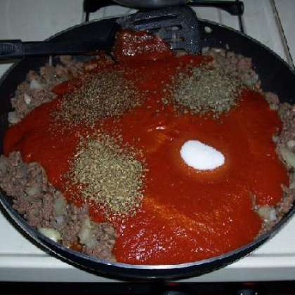 После того, как мясо поджарится, сбавьте огонь. Смешайте соус с орегано, перцем, базиликом и сахаром. Выливаем соус на фарш.