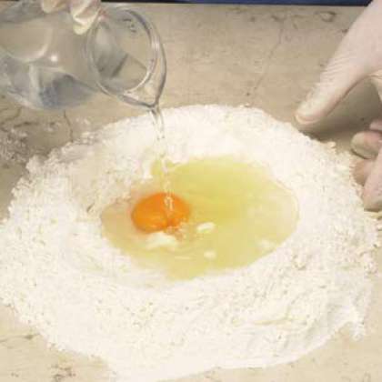 Сделайте колодец в центре муки, поместите яйцо внутрь и добавьте воду.