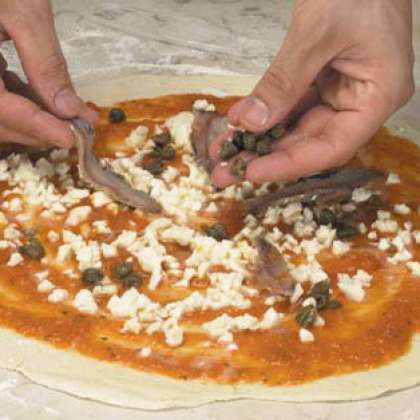 Разложите анчоусы и каперсы по поверхности пицци.