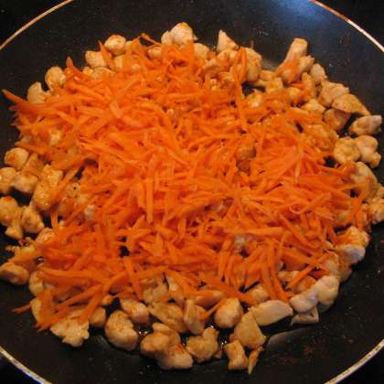 Добавить натёртую морковь к курице и перемешать. Поставить на медленный огонь и жарить 5-10 минут.