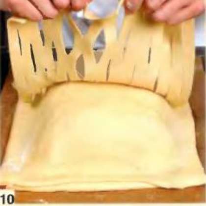 Аккуратно взять прорезанный пласт двумя руками, прикрыть им кулебяку, подтянуть края так, чтобы они сравнялись с краями кулебяки.