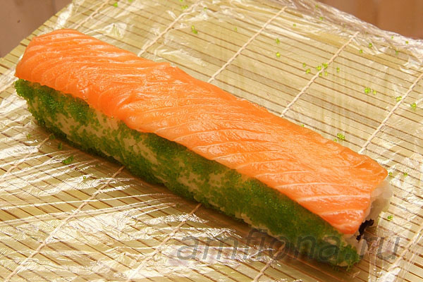 Положите на ролл несколько ломтиков лосося для суши и прижмите их ковриком. 