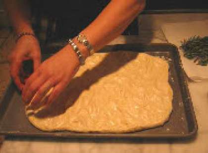 Распределите тесто пальцами по поверхности противня, оставив по краям расстояния в расчёте на то, что тесто поднимется ещё.