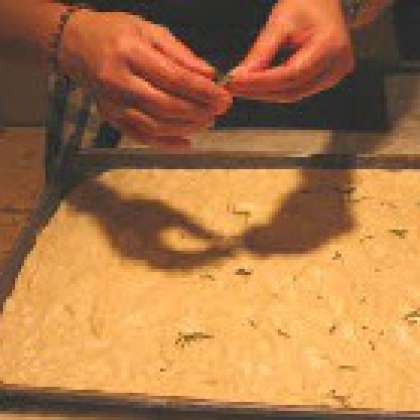 Накройте тесто плёнкой и отставьте настаиваться ещё час. Разогрейте духовку до 230 °С. Распределите равномерно по поверхности пирога листья розмарина (слегка вдавливая), крупную соль. Побрызгайте оставшимся оливковым маслом и отправьте в духовку.