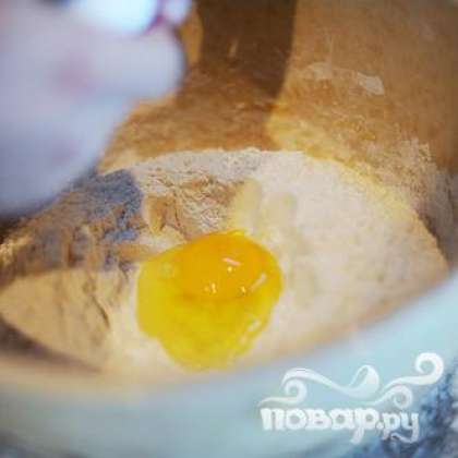 Всыпать муку в широкую миску. Посередине сделать небольшую ямку и разбить туда яйца.