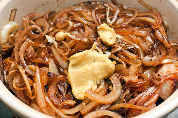 В толстостенную кастрюлю выложите мясо, сверху лук добавьте горчицу, соль и специи.