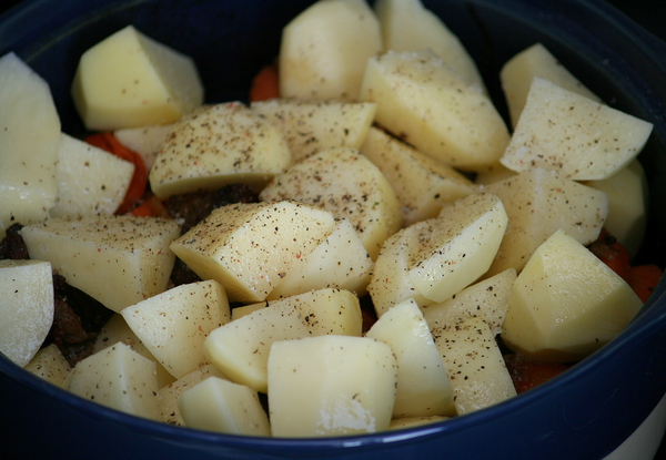 Через 40 минут достаем форму из духовки, добавляем картофель, солим, перчим по вкусу и осторожно перемешиваем: