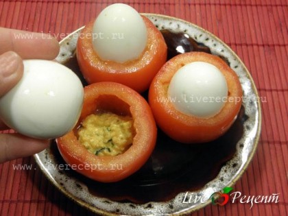 Берем подготовленные помидоры и кладем внутрь каждого по ложечке соуса, сверху вставляем очищенные вареные яйца.