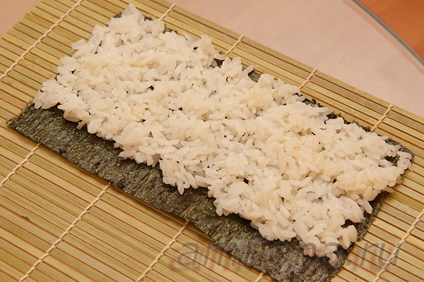 Влажными пальцами распределите рис по нори, оставив сантиметр или полтора свободным. Нанесите немного пасты васаби на рис.  