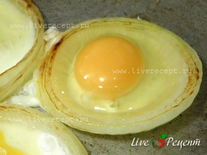 Сковороду с маслом разогреваем и выкладываем кольца лука. Поджариваем их с одной стороны, переворачиваем и выливаем в середину каждого яйцо.