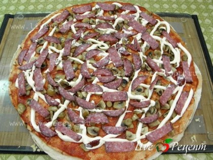 Далее немного майонеза и колбаса.Колбасу необходимо порезать, так как в дальнейшем пиццу будет легче нарезать.