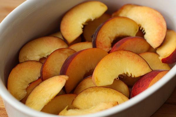 Большую форму или порционные формочки смажьте маслом и выложите туда дольки персиков в 1-2 слоя.