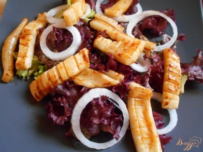 На блюдо выкладываем листья салата, полоски кальмаров, колечки лука и картофельные чипсы. Поливаем салат заправкой для салата.