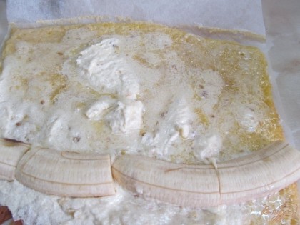 Вынуть из духовки готовое тесто и снять с противня прямо с пергаментом. Пусть чуть остынет (минут 15). Пласт смазать кремом (половина крема) и выложить банан.