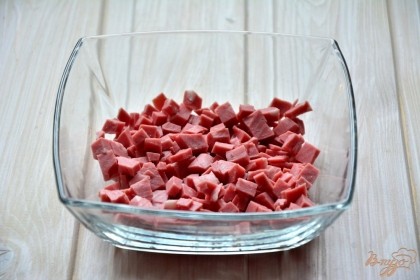 В салатник первым слоем выложить колбасу, нарезанную кубиком.