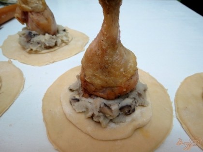 На меньший корж выкладываем столовую ложку картофельно - грибной начинки. На начинку устанавливаем куриную голень.
