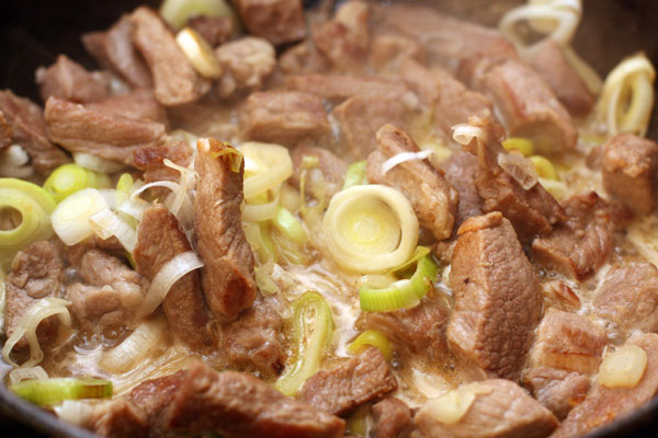 Обжарьте мясо на большом огне до образования румяной корочки. Выкладывайте мясо небольшими порциями, чтобы оно не дало сок раньше времени.  Затем добавьте нарезанный кольцами порей (белую часть), перемешайте, готовьте на среднем огне 2-3 минуты. 