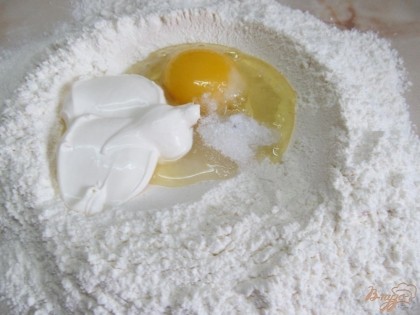 На рабочую поверхность высыпать муку и сделать внутри воронку. Туда вбить яйцо, добавить воду и сметану, посолить и высыпать сахар.