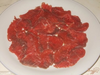 Для приготовления блюда выкладываем тоненькие кусочки говядины на плоское блюдо немного внахлест, но в один слой.