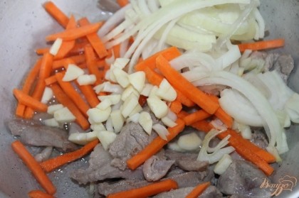 Добавить в сотейник к мясу морковь нарезанную соломкой, лук полукольцами и чеснок нарезанный средним кубиком. Обжарить.