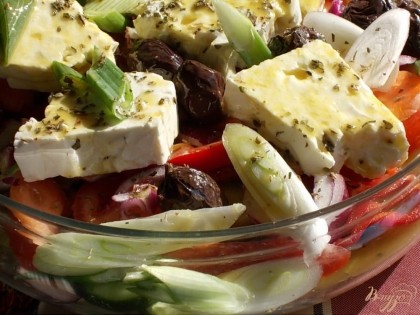 Выкладываем все овощи в салат и хорошо перемешиваем. Заливаем слат заправкой и еще раз перемешиваем. Сыр фету выкладываем сверху, добавляем оливки и орегано с базиликом.