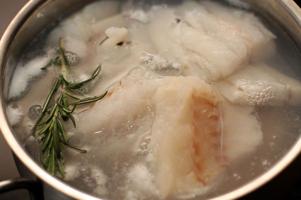 Филе рыбы опустите в кипящую подсоленную воду вместе с веточкой розмарина. Доведите до кипения, затем воду слейте.