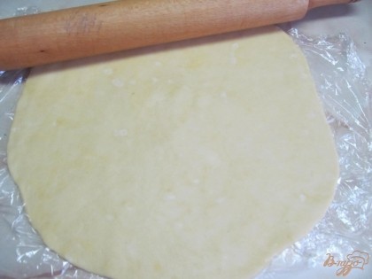 Вынимаем тесто и прямо на пищевой пленке раскатываем до размера формы, учитывая борта. У меня форма 25 см. в диаметре.