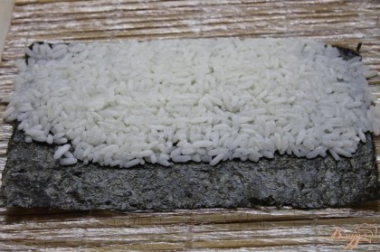 Рис положить на лист нори и прижать его сильно с помощью бамбукового коврика.