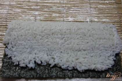 Рис положить на нори и хорошо прижать бамбуковым ковриком.