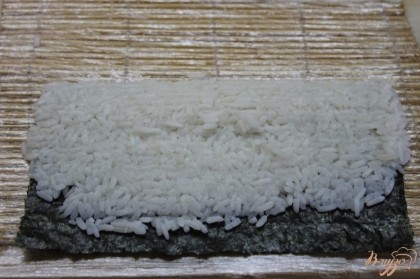 На лист нори положить готовый рис и зажать его с помощью бамбукового коврика.