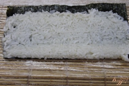 Выложить рис на лист нори и хорошо прижать его с помощью бамбукового коврика.