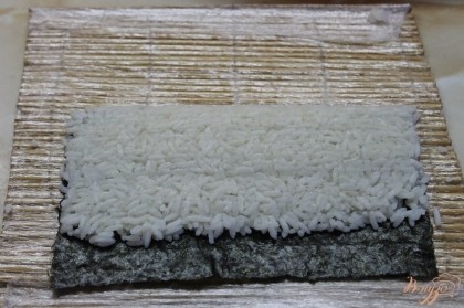 Готовый остывший и заправленный рис выложить на лист нори и хорошо сжать с помощью бамбукового коврика.
