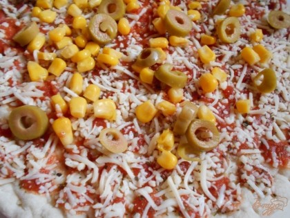 Если у вас нет готовой заготовки для пиццы или вы привыкли готовить тесто сами, тогда приготовьте основу для пиццы по своему рецепту. Смажем основу кетчупом и распределим немного тертого твердого сыра по поверхности пиццы. Сверху выкладываем консервированную кукурузу и оливки.