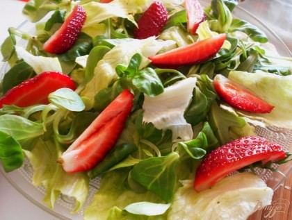 На плоское блюдо выкладываем смесь салатных листьев, сверху кладем кусочки клубники.